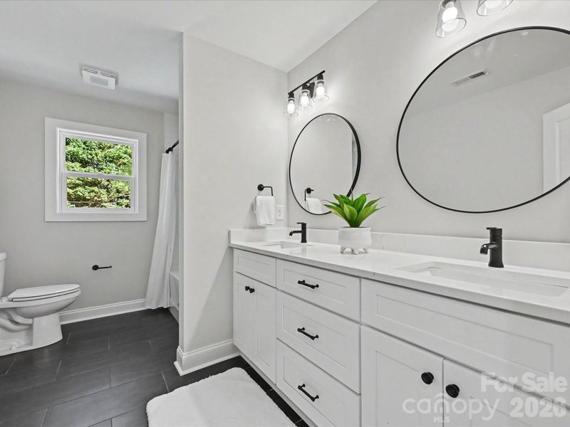Stylish full bath features a dual-sink vanity, sleek black fixtures, and a bright, modern design with ample storage space.