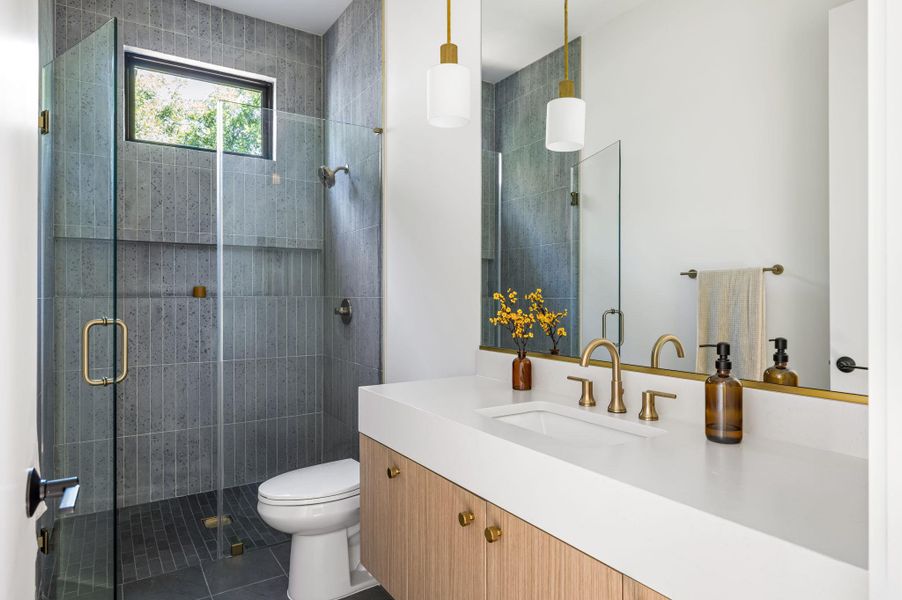 A contemporary vanity with a white countertop complements a sleek glass-enclosed walk-in shower.