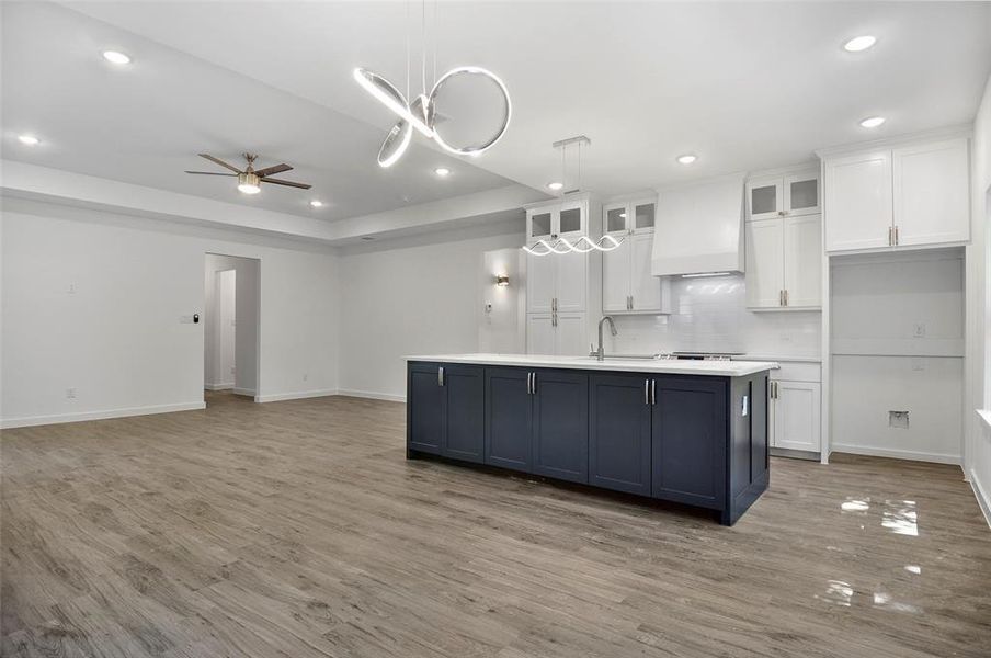 Kitchen with backsplash, light hardwood / wood-style flooring, custom exhaust hood, and an island with sink