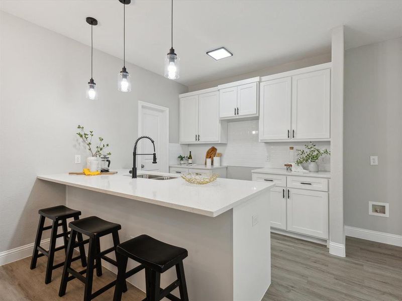 Kitchen featuring light wood-type flooring, hanging light fixtures, white cabinetry, and sink