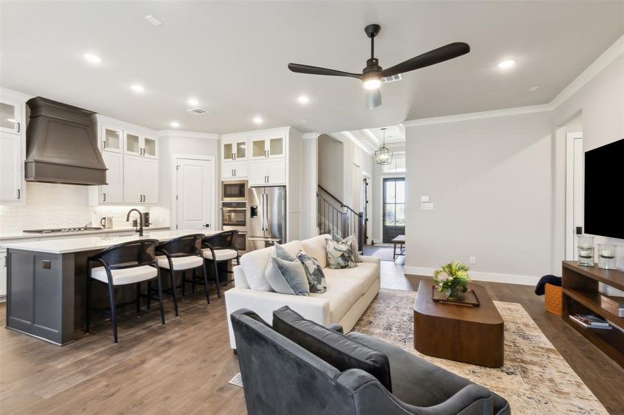 Living room featuring ceiling fan with notable chandelier, crown molding, and dark wood-type flooring