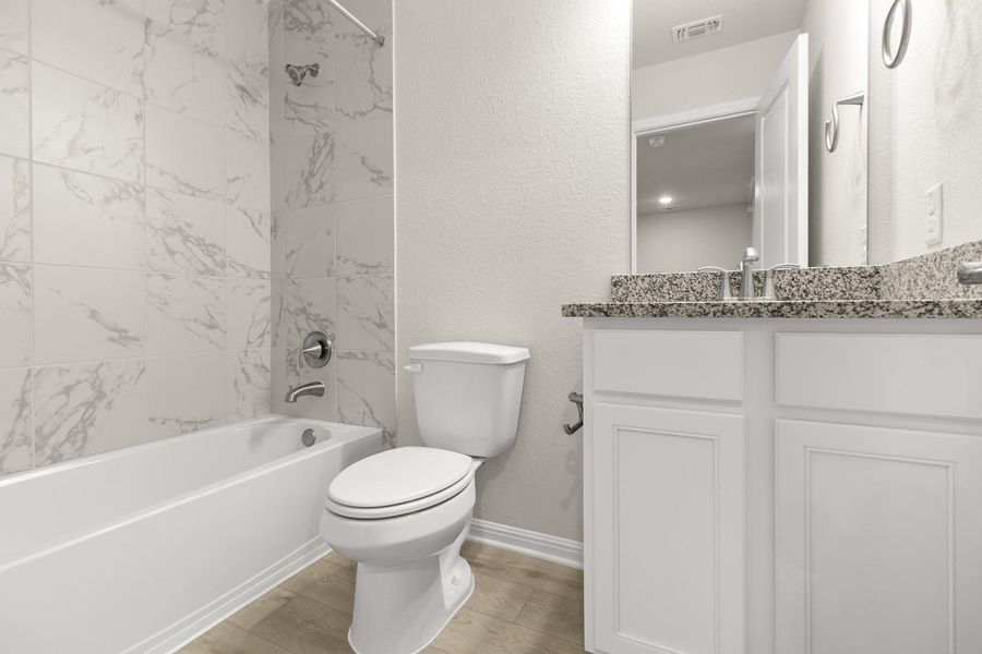 Bathroom featuring a white vanity with a granite countertop, a bathtub with a tiled surround, and wood-look flooring