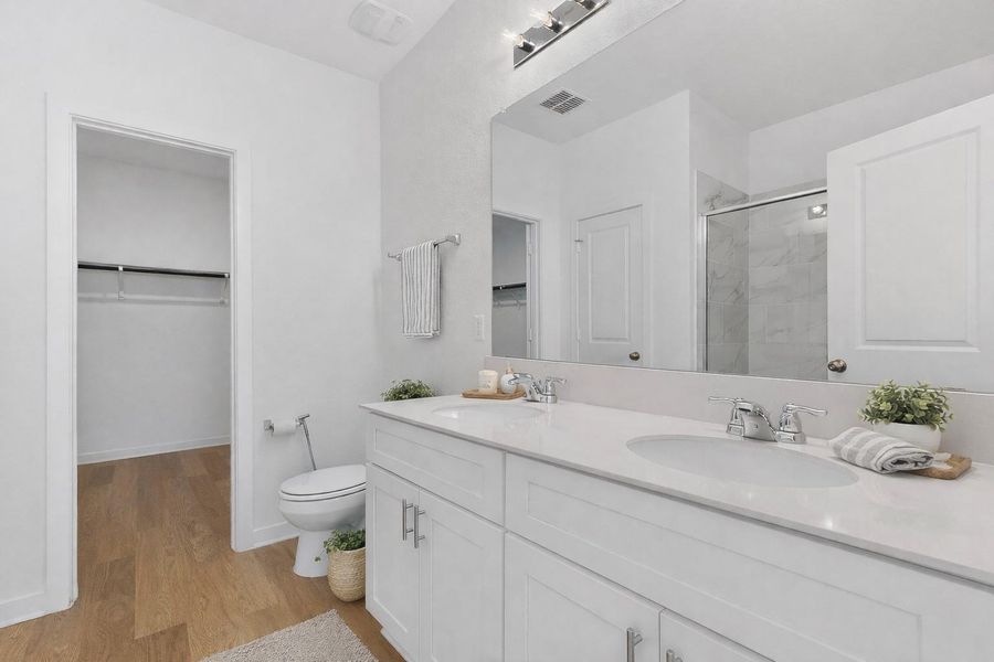 Bathroom with double vanity, light wood finished floors, a spacious closet, and a stall shower