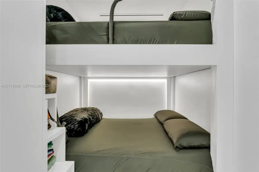 Built-in white stacked bunk structure featuring integrated shelving and recessed LED accent lighting Built-in white stacked bunk structure featuring integrated shelving and recessed LED accent lighting