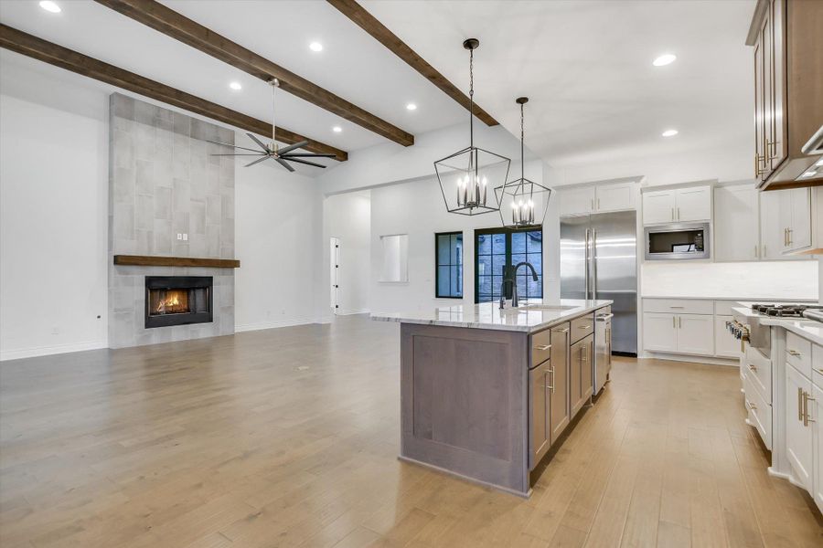 Kitchen with built in appliances, white cabinetry, beam ceiling, light stone countertops, and light wood-type flooring