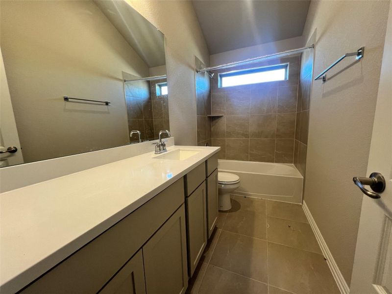 Full bath featuring vanity, a textured wall, shower / washtub combination, and dark tile patterned flooring