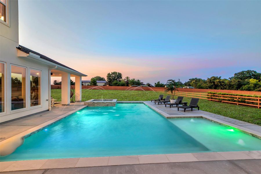 Twilight Elegance: As the sun dips below the horizon, the pool glows with cascading water features and ambient lighting, transforming the backyard into an evening sanctuary. Expansive decking invites alfresco lounging, while the spa and covered patio extend the home’s resort-inspired lifestyle.