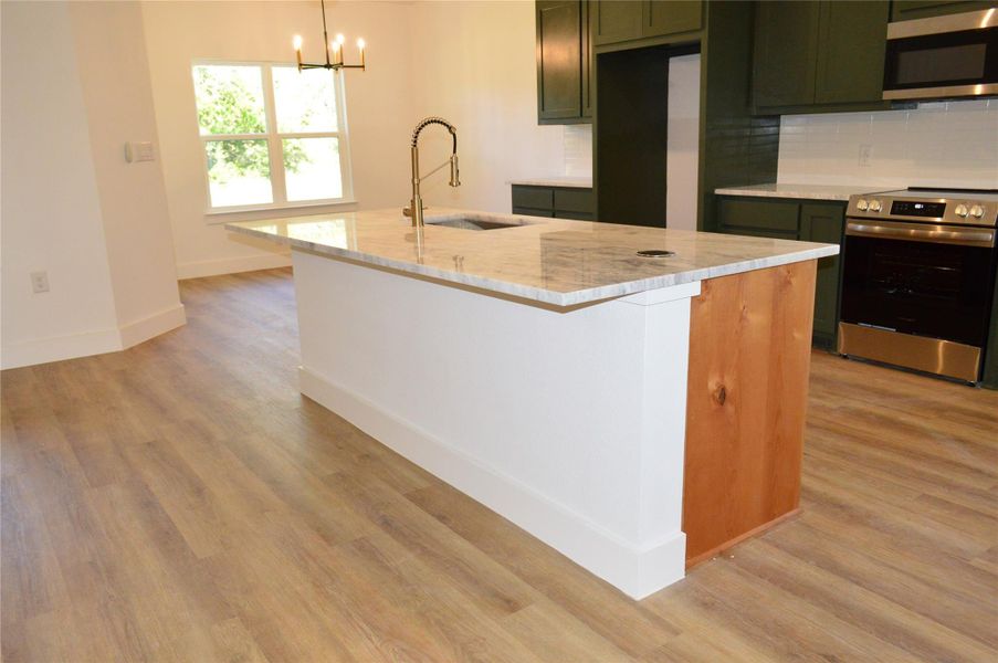 Kitchen with stainless steel appliances, decorative backsplash, green cabinetry, light stone countertops, and an island with sink Kitchen with stainless steel appliances, decorative backsplash, green cabinetry, light stone countertops, and an island with sink