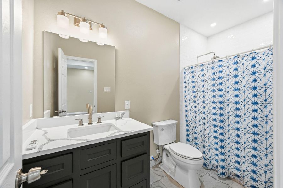 This beautifully designed primary bathroom offers a clean, modern aesthetic with upscale finishes throughout. The sleek vanity features rich dark cabinetry paired with bright quartz-style countertops and contemporary fixtures, creating a striking contrast.