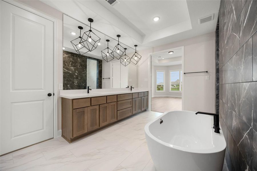 Another spectacular view of the primary ensuite bathroom, highlighting the massive length of the double-sink vanity and its premium storage options. This angle captures the seamless flow into the primary bedroom suite and showcases the elegant tray ceiling details above. A wall-to-wall vanity mirror reflects the striking geometric pendant lighting and dark marble-look tile features. Another spectacular view of the primary ensuite bathroom, highlighting the massive length of the double-sink vanity and its premium storage options. This angle captures the seamless flow into the primary bedroom suite and showcases the elegant tray ceiling details above. A wall-to-wall vanity mirror reflects the striking geometric pendant lighting and dark marble-look tile features.
