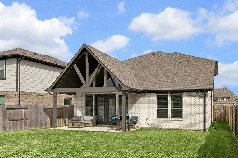 THE REAR EXTERIOR SHOWS THE LARGE GABLED ROOF OF THE COVERED PATIO AND THE BRICK SIDING OF THE HOME.