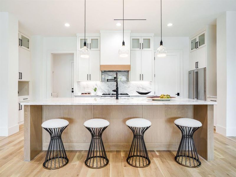 Kitchen featuring glass fronted cabinets, a breakfast bar, light stone counters, and light wood-style floors