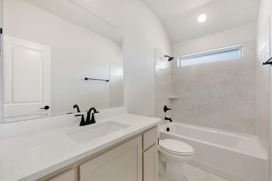 Bathroom with white quartz vanity, black fixtures, tub-shower combo with tile surround, and vaulted ceiling