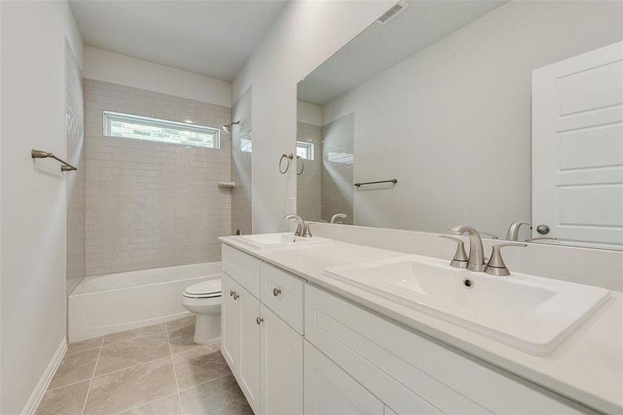 Full bathroom with tile patterned floors, double vanity, tiled shower / bath, and toilet