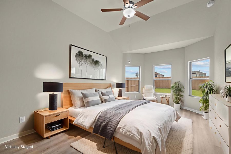 A well-lit bedroom with vaulted ceilings and large windows overlooks a private yard.