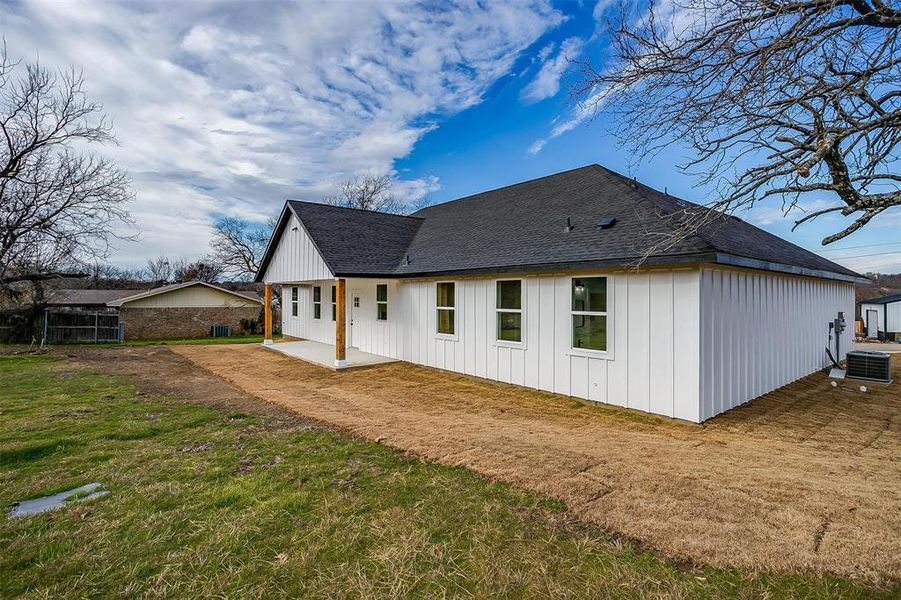 Rear view of house with board and batten siding, cooling unit, a patio area, and roof with shingles Rear view of house with board and batten siding, cooling unit, a patio area, and roof with shingles