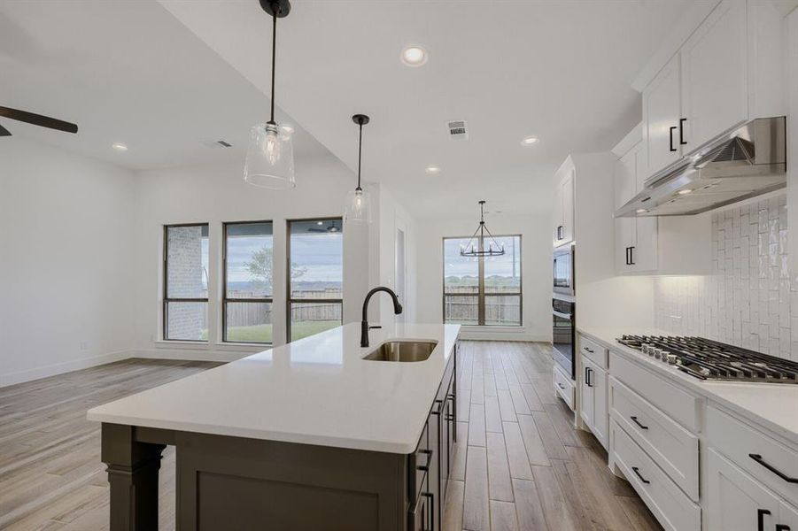 Spacious kitchen featuring a dark-toned island with an undermount sink, quartz countertops, white cabinetry, a gas cooktop, and double wall ovens