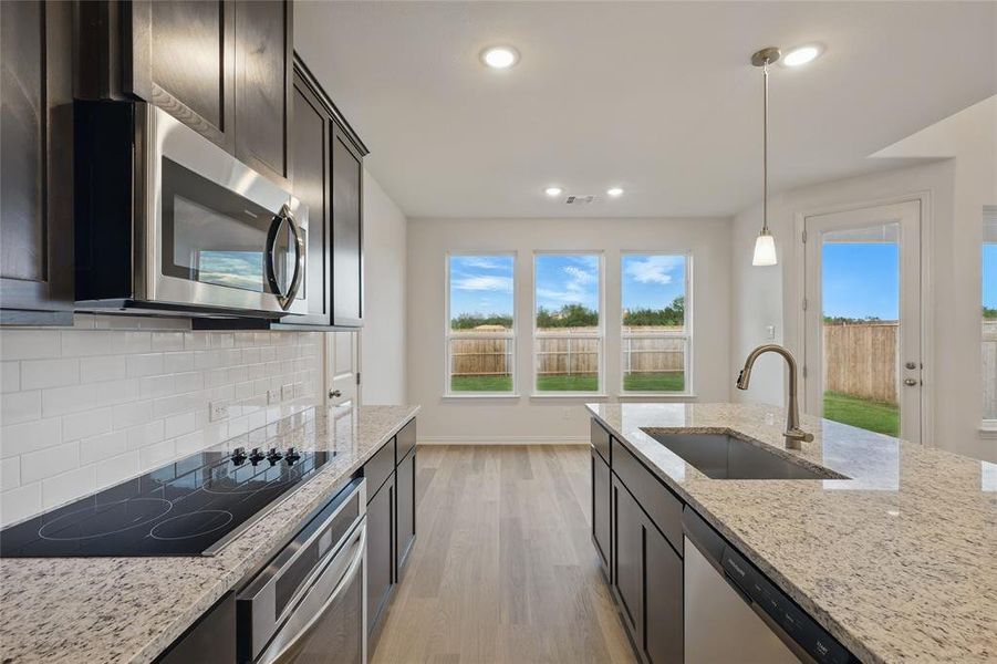 Kitchen featuring a sink, appliances with stainless steel finishes, light wood finished floors, decorative backsplash, and light stone counters Kitchen featuring a sink, appliances with stainless steel finishes, light wood finished floors, decorative backsplash, and light stone counters
