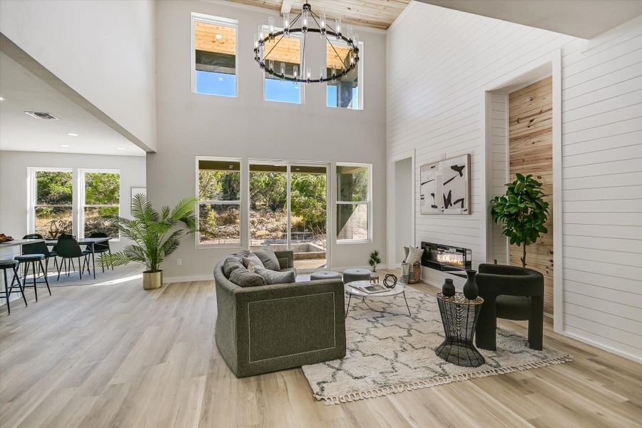 A spacious living room features soaring ceilings, a striking chandelier, and natural light from many windows.