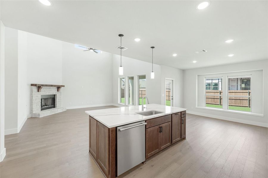 Open-concept kitchen and living area with center island, stone fireplace, hardwood floors, and vaulted ceiling Open-concept kitchen and living area with center island, stone fireplace, hardwood floors, and vaulted ceiling