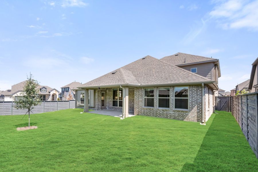 Brick home rear exterior with covered patio, large green backyard, and wood privacy fence