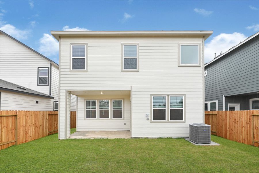 This photo showcases the back view of a modern two-story home. It features a covered back patio, a neatly maintained lawn, and a wooden privacy fence. The house includes multiple windows for natural light and an exterior HVAC unit.Please note: The image is not the actual home; it is a home with the same floor plan in the neighborhood. Finishes may vary. This photo showcases the back view of a modern two-story home. It features a covered back patio, a neatly maintained lawn, and a wooden privacy fence. The house includes multiple windows for natural light and an exterior HVAC unit.Please note: The image is not the actual home; it is a home with the same floor plan in the neighborhood. Finishes may vary.