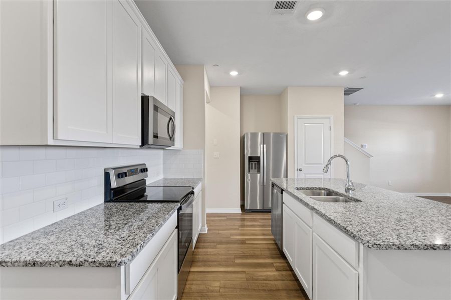 Kitchen with stainless steel appliances, light stone counters, a center island with sink, dark wood-style floors, and white cabinets Kitchen with stainless steel appliances, light stone counters, a center island with sink, dark wood-style floors, and white cabinets