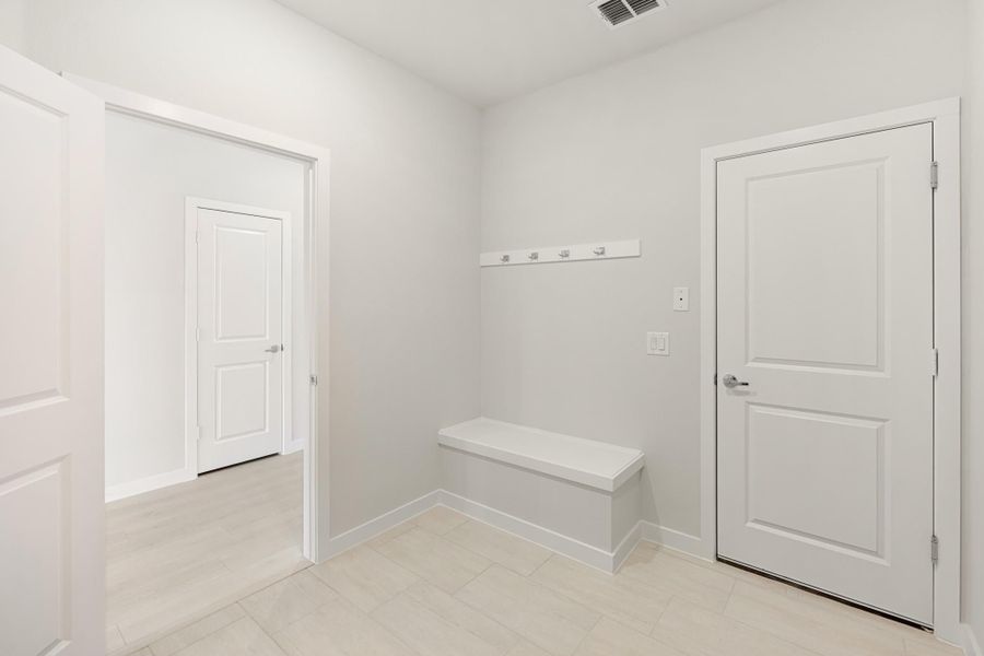 Mudroom with built-in bench, wall coat hooks, and white doors on tile floor