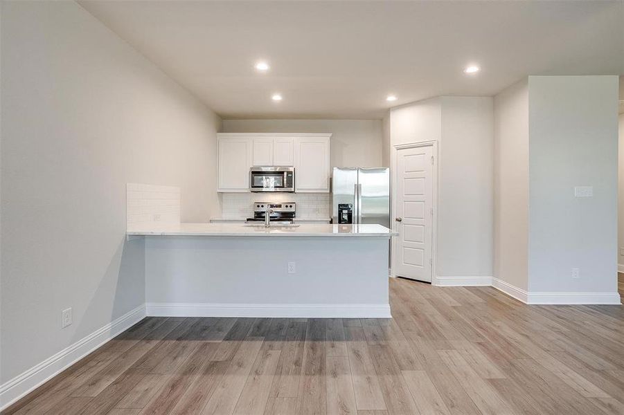 Kitchen with light wood finished floors, a peninsula, appliances with stainless steel finishes, and decorative backsplash