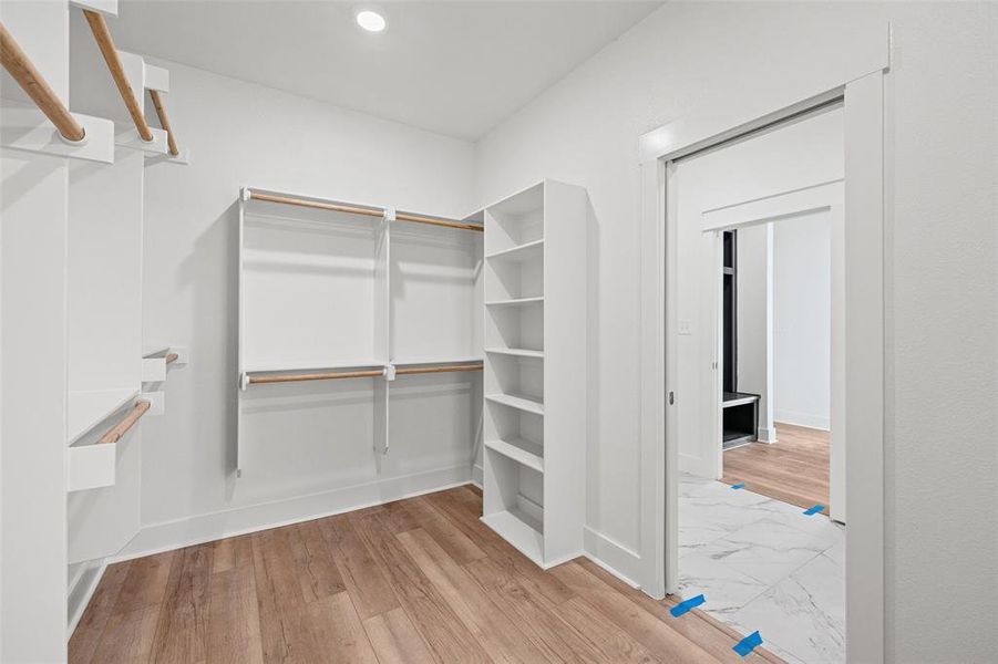 Spacious walk-in closet featuring wood-finish flooring, white walls, recessed ceiling lighting, built-in shelving, and multiple hanging rods