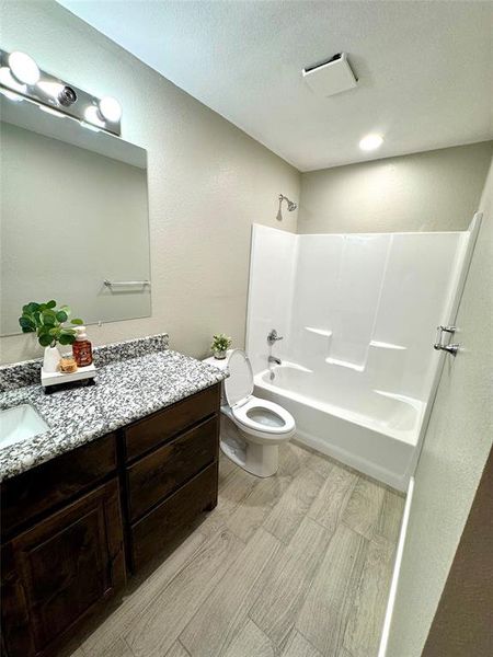 Bathroom with shower / bath combination, vanity, a textured wall, and light wood-style floors