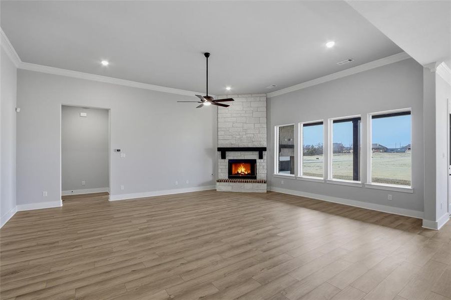Unfurnished living room with a stone fireplace, ceiling fan, ornamental molding, recessed lighting, and light wood-type flooring