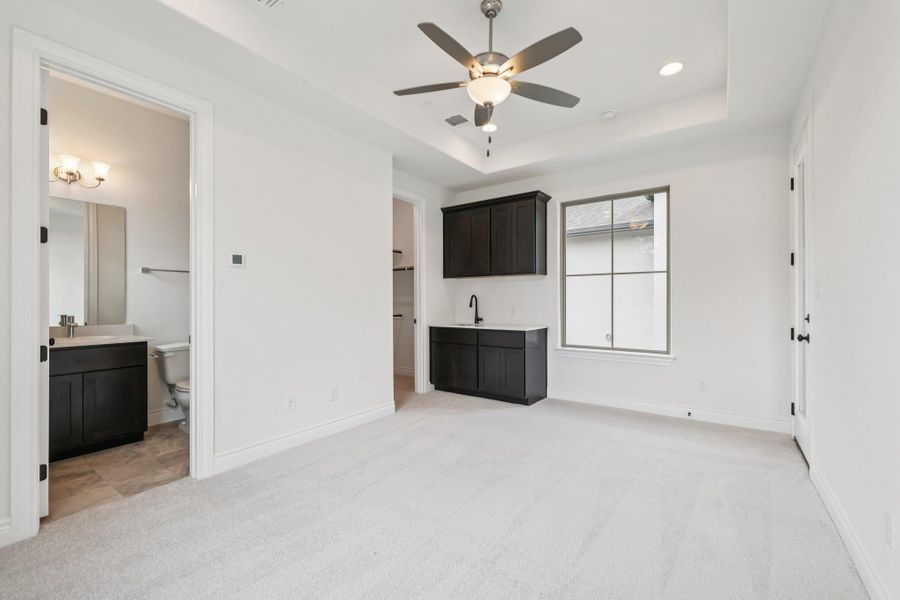 Unfurnished bedroom with light colored carpet, a tray ceiling, a ceiling fan, ensuite bathroom, and recessed lighting