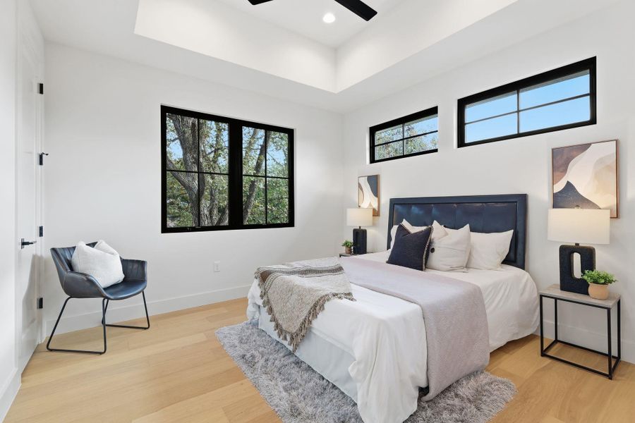 Bedroom with a raised ceiling, light wood-style flooring, a ceiling fan, and recessed lighting