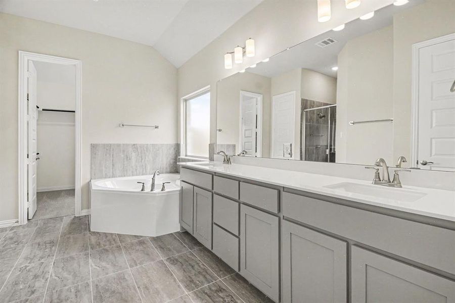 Spacious bathroom featuring a corner soaking tub, dual vanities with white countertops, and expansive mirror Spacious bathroom featuring a corner soaking tub, dual vanities with white countertops, and expansive mirror