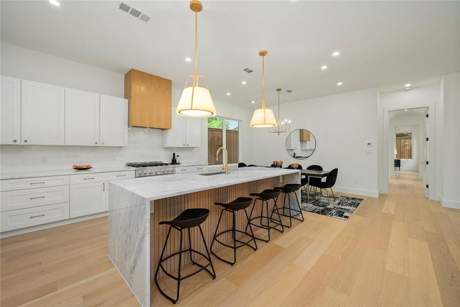 Modern kitchen featuring light wood flooring, white cabinetry, a marble-topped island with a fluted wood base, and gold-toned pendant lighting