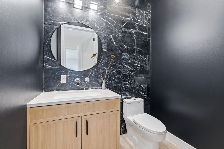 A striking powder room features a marble-tiled accent wall and a contemporary vanity with a wall-mounted faucet. A striking powder room features a marble-tiled accent wall and a contemporary vanity with a wall-mounted faucet.