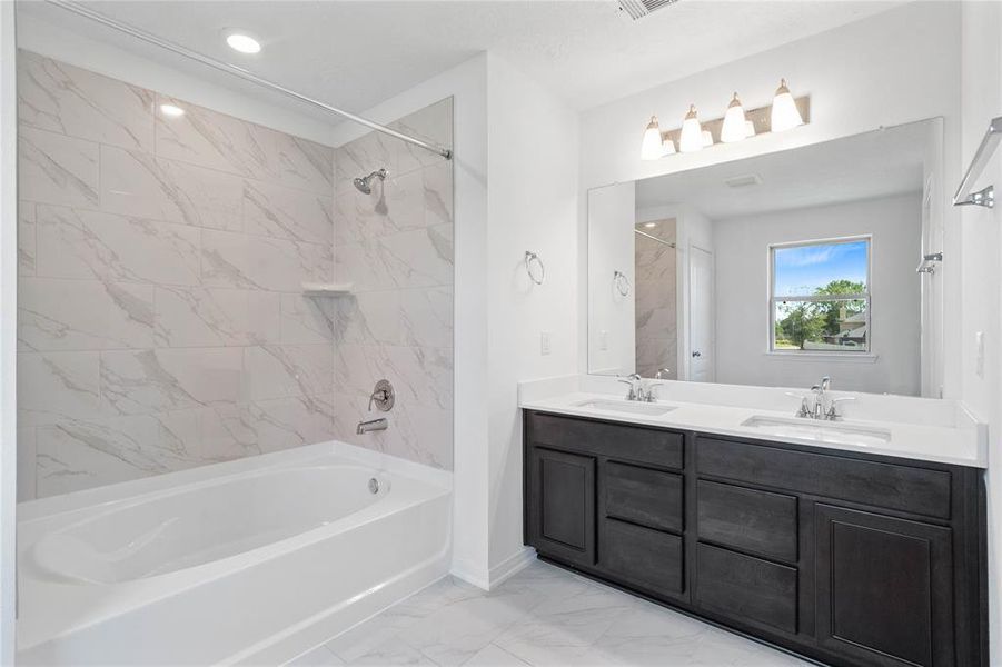 This primary bathroom is definitely move-in ready! Featuring an oversized tub and shower combo with tile surround, stained cabinets with light countertops, dual vanities, high ceilings, neutral paint, sleek and modern finishes.