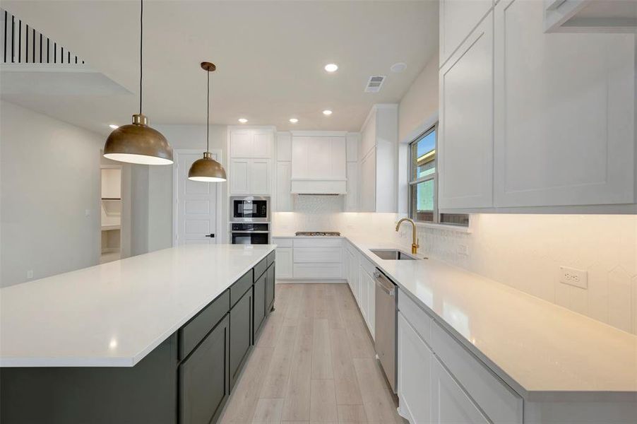 Kitchen featuring two tone cabinets, tasteful backsplash, light wood finished floors, hanging light fixtures, and light stone counters