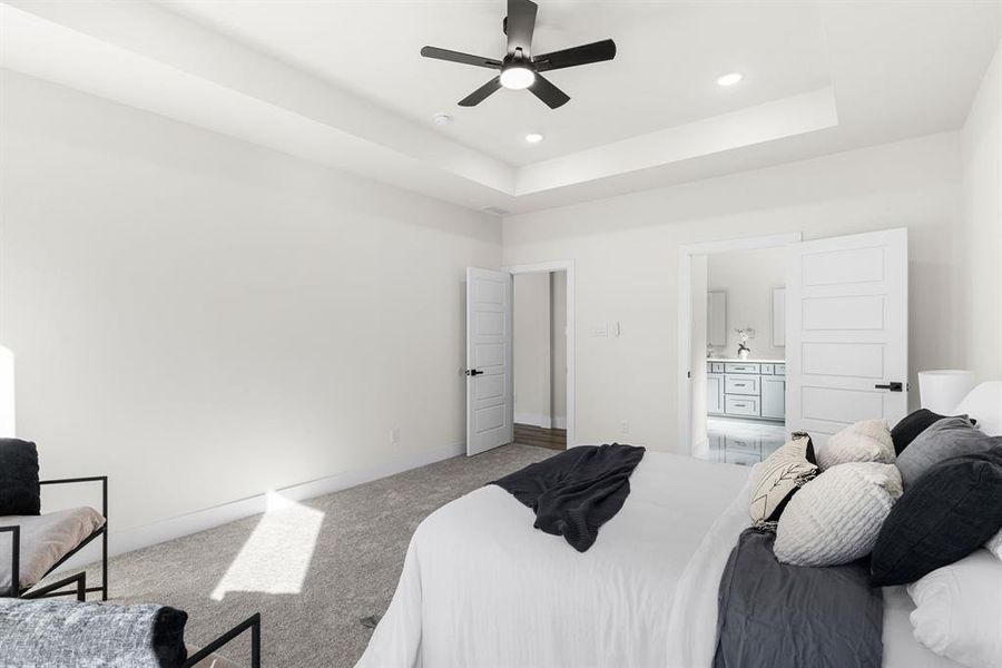 Bedroom with ceiling fan, a raised ceiling, carpet floors, and ensuite bath