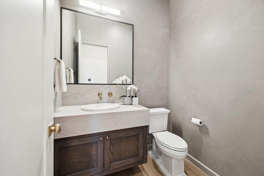 This sleek powder room showcases a modern vanity with dark wood cabinetry, a Azzura Bay marble countertop with leather finish, and minimalist fixtures. The wall-mounted faucet and round sink add a contemporary touch to this elegant space.