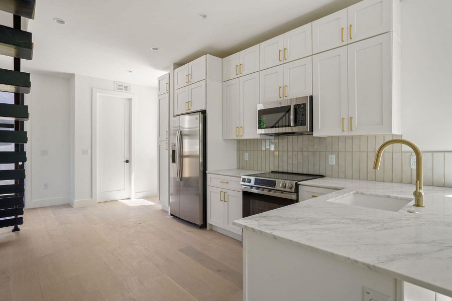Kitchen featuring light stone countertops, light wood-style flooring, tasteful backsplash, appliances with stainless steel finishes, and a sink