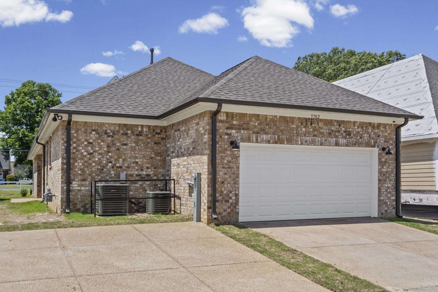 Brick exterior with a white garage door, dark shingle roof, and concrete driveway