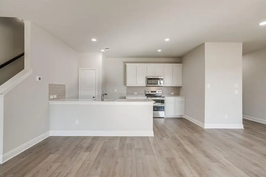 Kitchen featuring white cabinets, stainless steel appliances, a peninsula, light wood-style floors, and recessed lighting