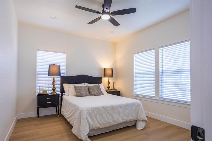 Bedroom with light wood-style flooring, a ceiling fan, and multiple windows
