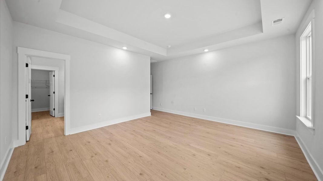 Elegant primary suite with hardwood flooring, tray ceiling, and superior natural light in this accomplished DRB Homes design