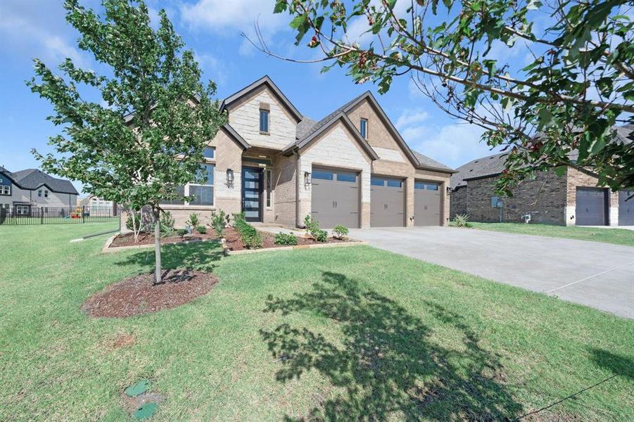 View of front facade with driveway, brick and stone siding, landscaping, and an attached 3-car garage on a large lot.