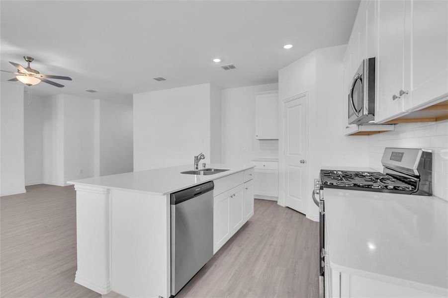 Kitchen with a kitchen island with sink, sink, stainless steel appliances, and white cabinets