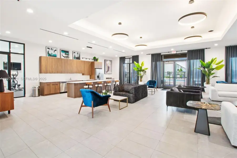 Expansive common area featuring wood-finish cabinetry, a large kitchen island, recessed tray ceiling lighting, oversized tile flooring, and floor-to-ceiling glass panel entryways
