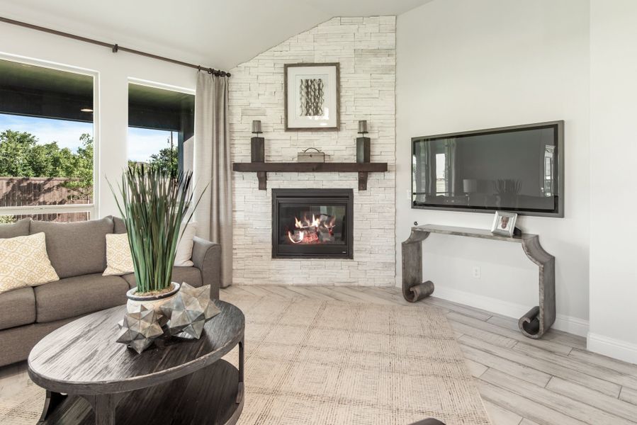 Living room with white stacked stone fireplace, wood mantel, wall-mounted TV, and gray sofa near large windows